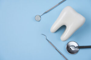 Picture of a white tooth figure, a stethoscope, and two dental instruments against a light blue background.