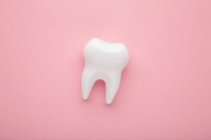 Picture of a white tooth figure against a light pink background.