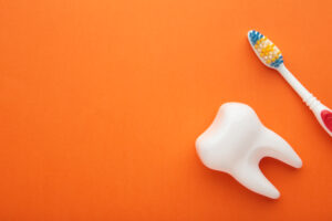Picture of a white tooth figure and a toothbrush against an orange background.